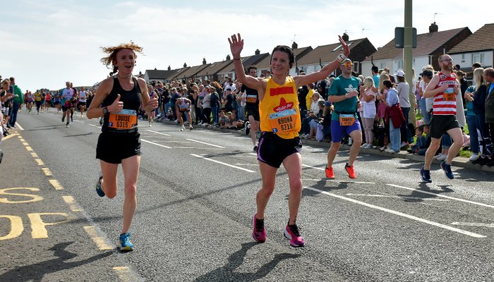 Rhona, woman in Action for Children t-shirt, cheers to the crowd as she runs the great north run for Action for Children