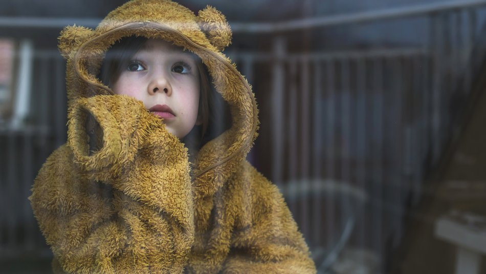 Sad cold child wearing yellow jumper looking out window