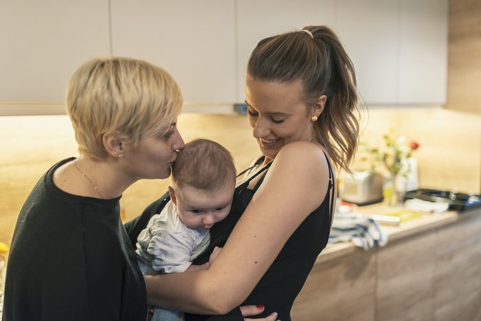 Same sex couple, two women playing with their 6 month old baby boy at home while standing in kitchen