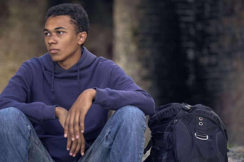 Boy sitting on ground with rucksack - boy has a cut to his face