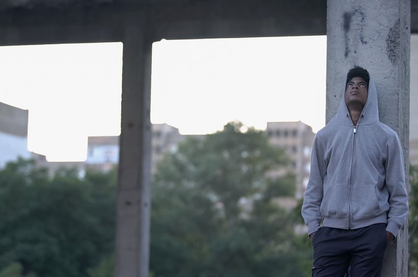 Boy standing amongst concrete pillars - trees surround - he looks up at sky