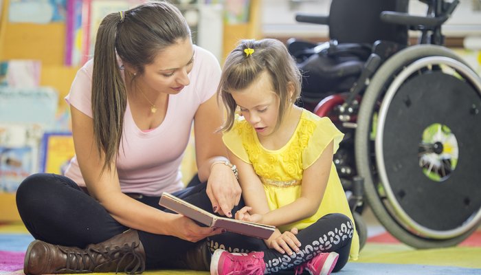 Teacher and young girl sitting on the ground reading a book together.jpg
