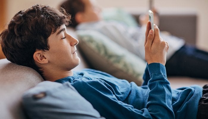 Teen boy sitting on sofa in living room using a mobile phone