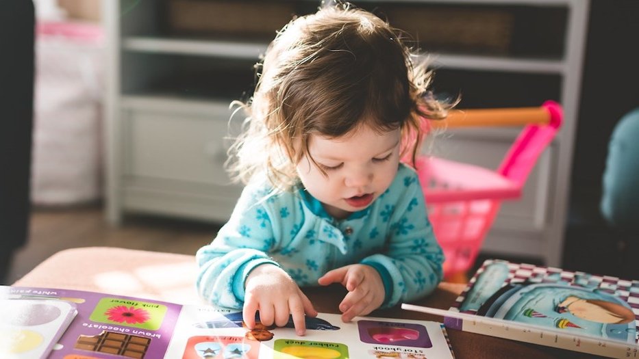 Toddler sat at coffee table reading childrens books