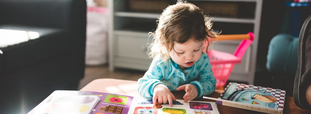 Toddler sat at coffee table reading childrens books