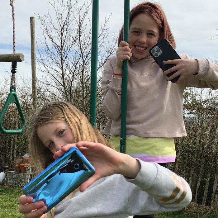 Two young girls on a swing set holding their mobile phone cameras to take a picture