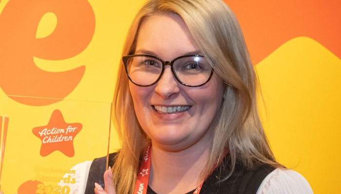 Woman holding up Stephenson Awards plaque in front of Action for Children banner