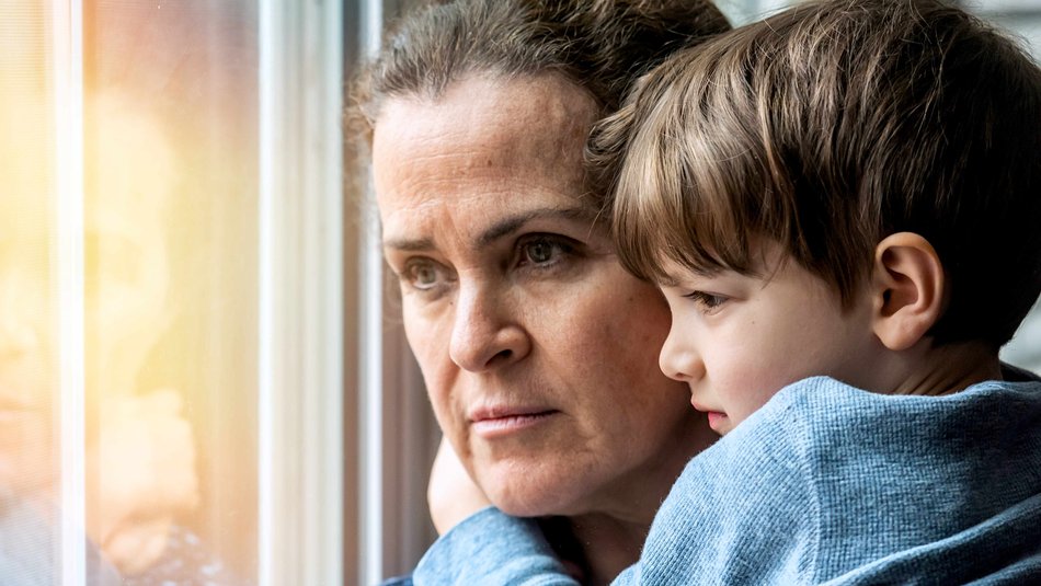 Worried looking mum holding son and looking out the window