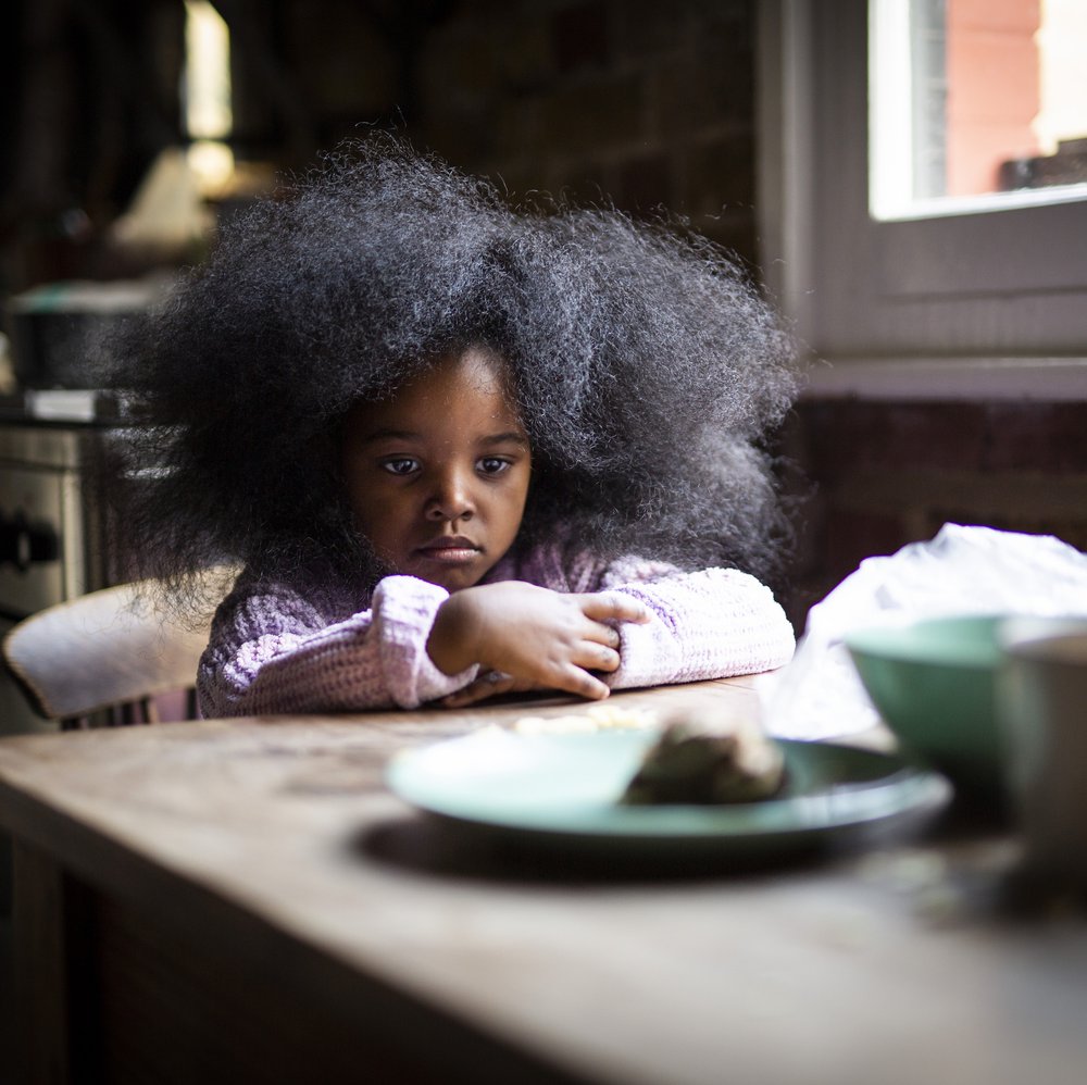 Worried young girl sits at table with empty plate
