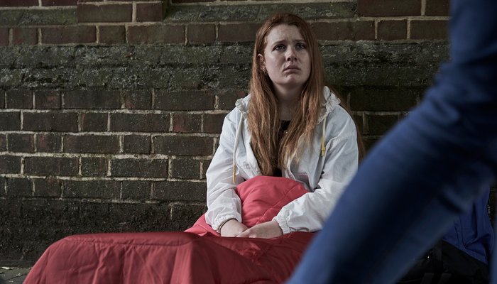 youg homeless girl sitting in sleeping back on street floor as people walk past.jpg