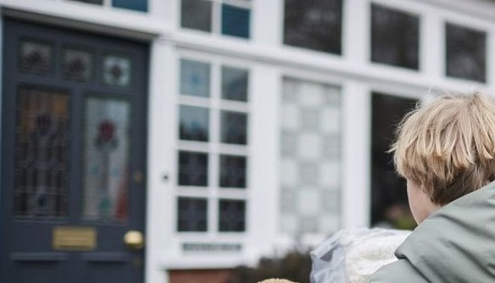 Young boy approaching new foster home whilst holding teddy bear