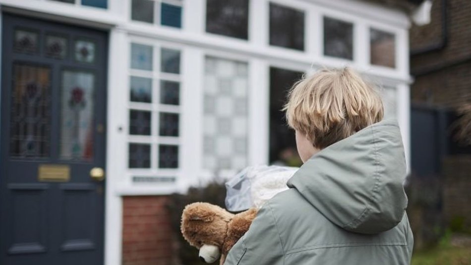 Young boy approaching new foster home whilst holding teddy bear