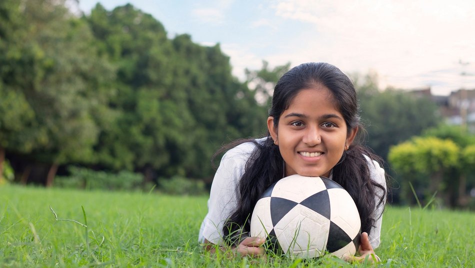 Young girl laying on the grass with a football, smiling into the camera