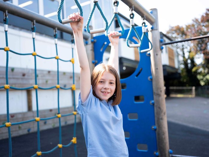 Young girl hanging from school playground monkey bars and smiling