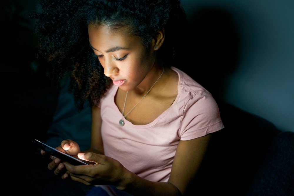 young girl sitting on bed using smartphone at night
