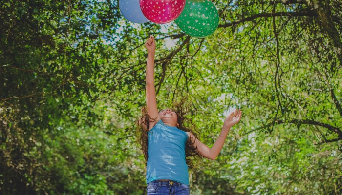 Young happy girl jumping in the air to catch balloons in park