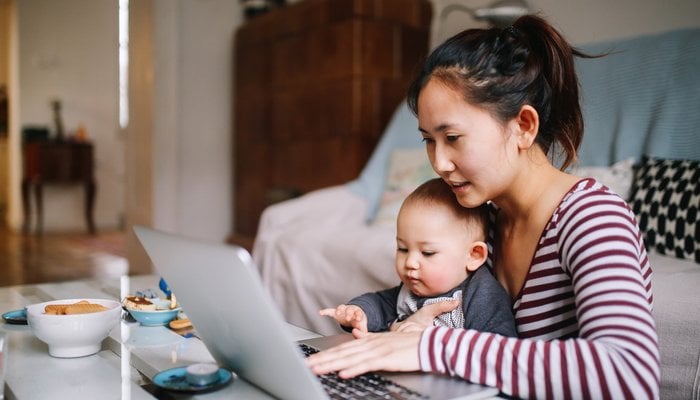 Young mother working on laptop with son in her lap