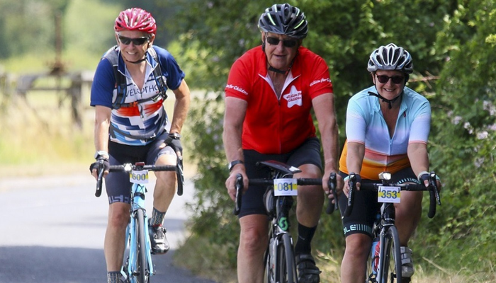 Three people on cycling. Person in the middle is wearing an Action for Children cycling t-shirt