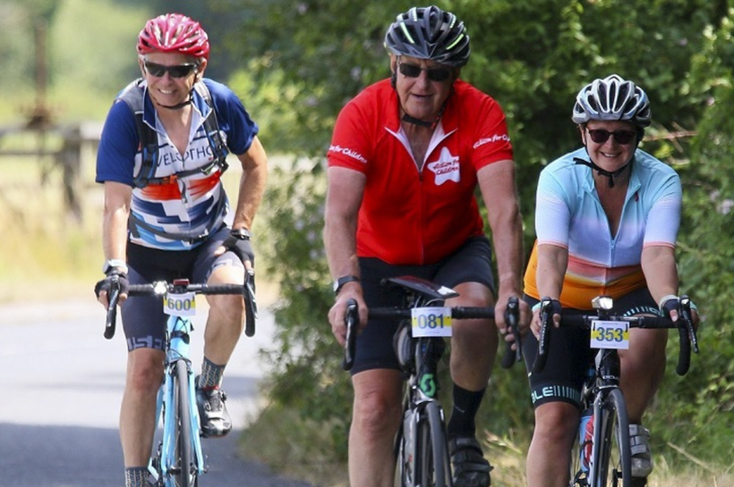 Three people on cycling. Person in the middle is wearing an Action for Children cycling t-shirt