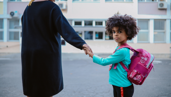 Young girl holding her mum's hand looks back at camera with a straight face